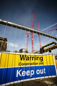 warning sign at construction site with multiple cranes working in the background